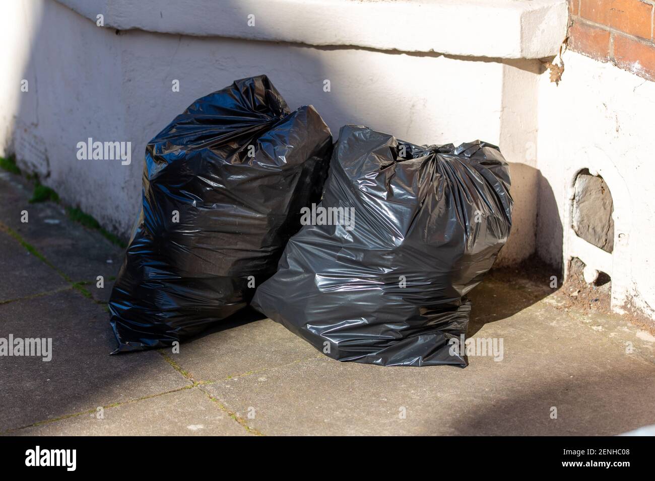 Two full black rubbish bags or black bin bags outside a house ready for bin collection Stock Photo