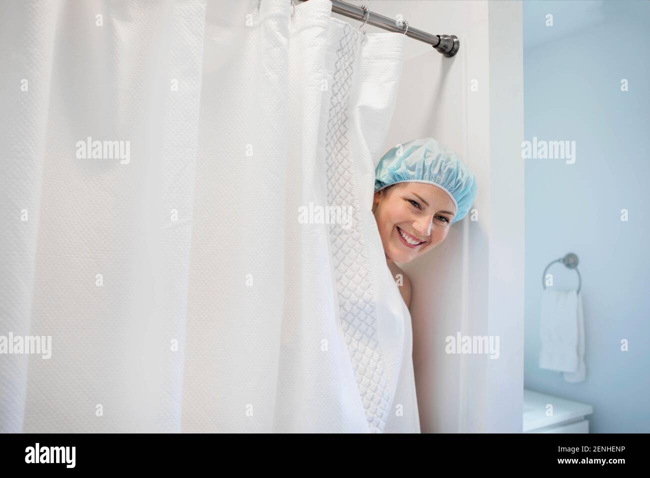 A woman smiles as she peeks out of a shower stall wearing a shower cap. Stock Photo