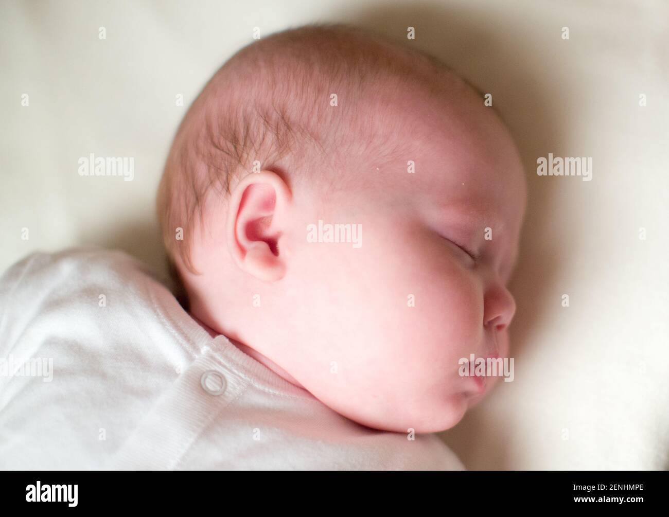 Sleeping newborn baby in cot and baby grow Stock Photo
