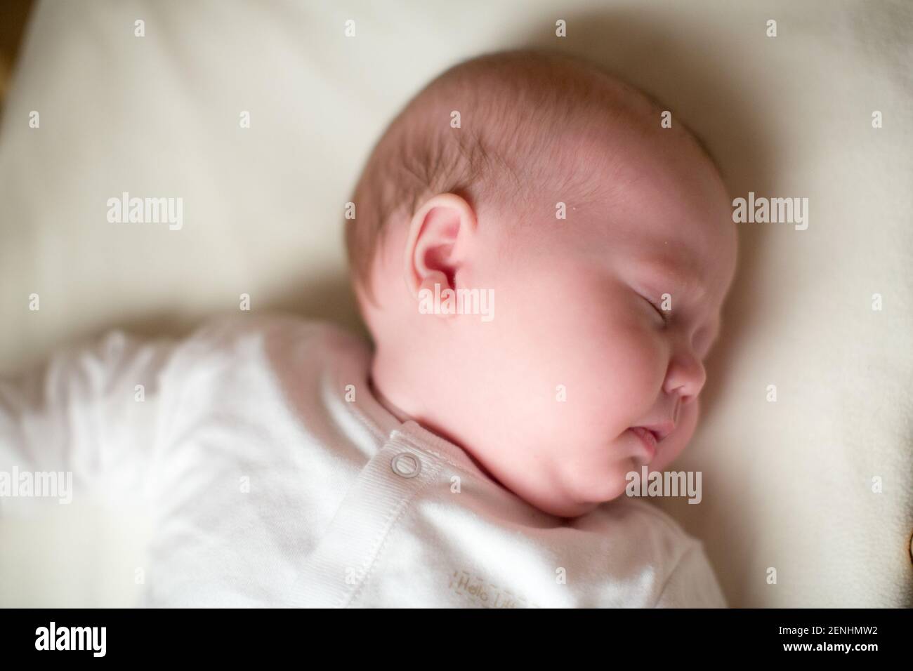 Sleeping newborn baby in cot and baby grow Stock Photo