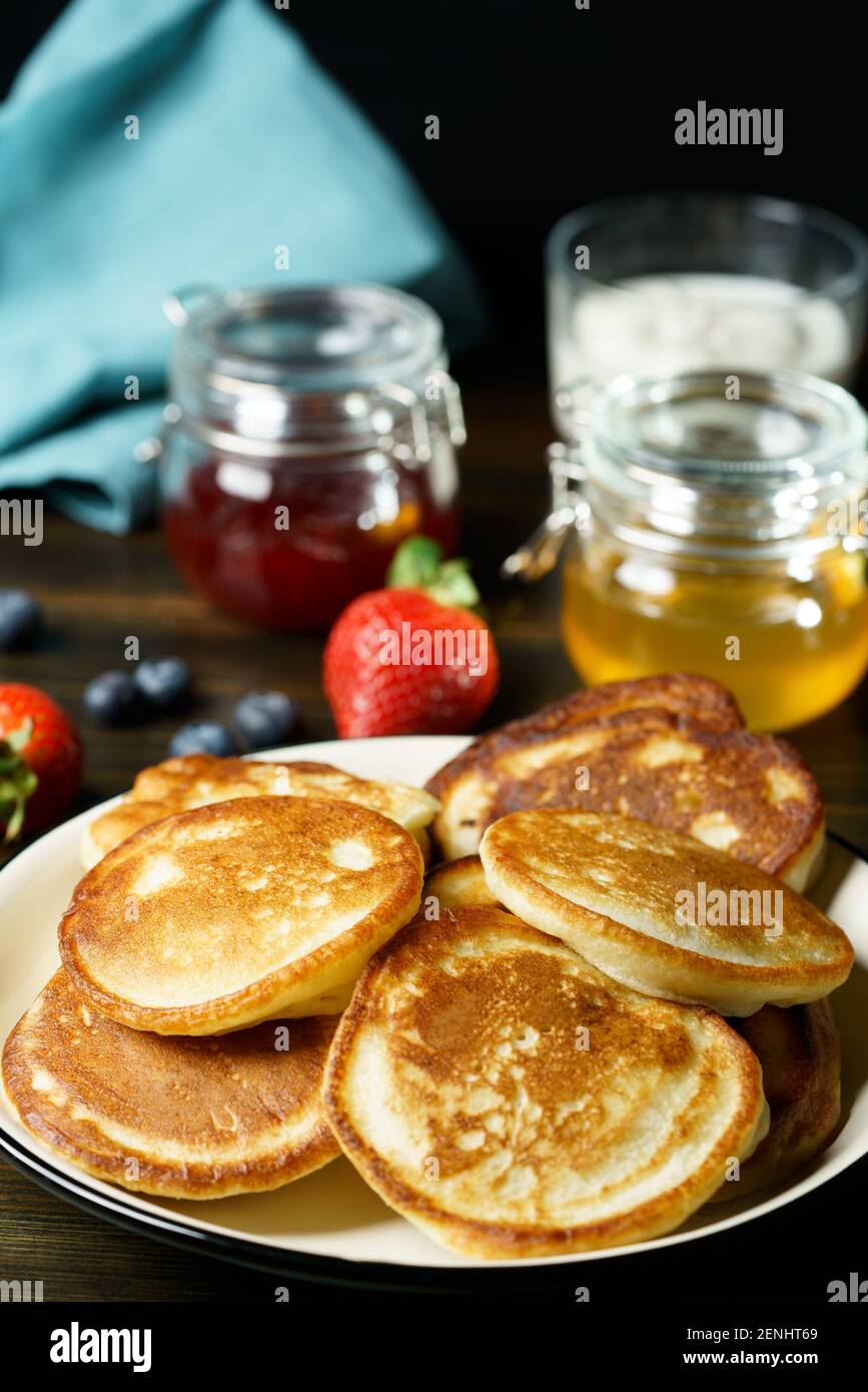 Blini served with strawberry jam, honey, sour cream and fresh berries. Dark wooden table, high resolution Stock Photo