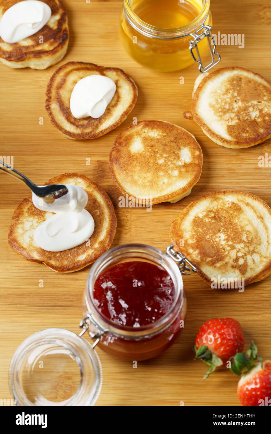 Blini served with strawberry jam, honey, sour cream and fresh berries. Wooden board, high resolution Stock Photo