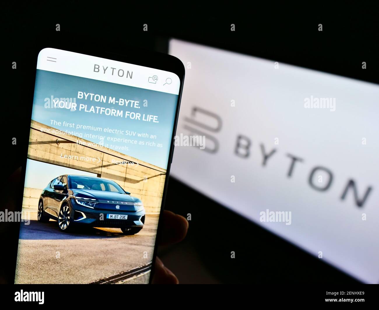 Person holding mobile phone with logo of Chinese automotive brand Byton on screen in front of business web page. Focus on center of phone display. Stock Photo