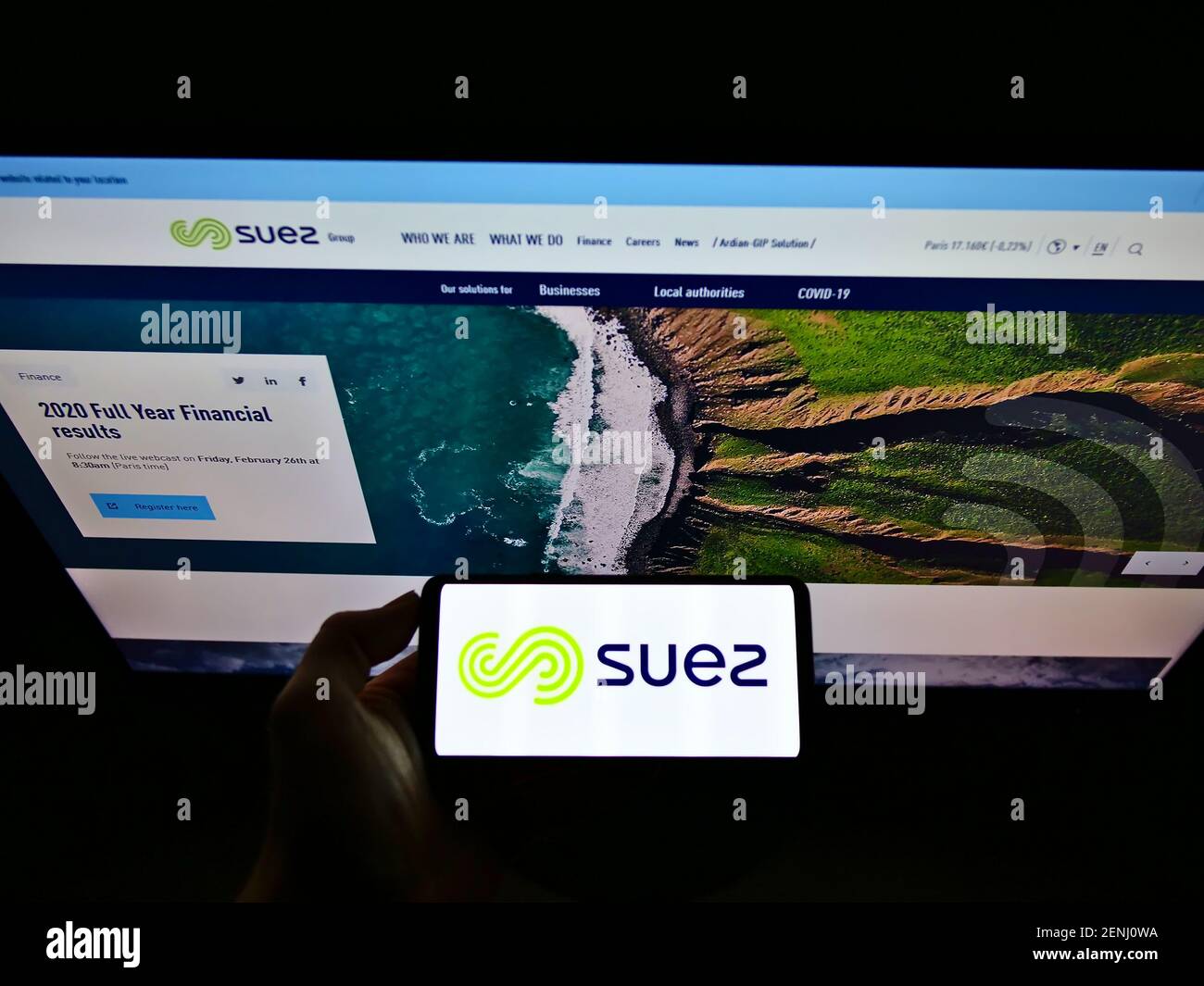 Person holding smartphone with logo of French utility company Suez S.A. on screen in front of website. Focus on phone display. Unmodified photo. Stock Photo
