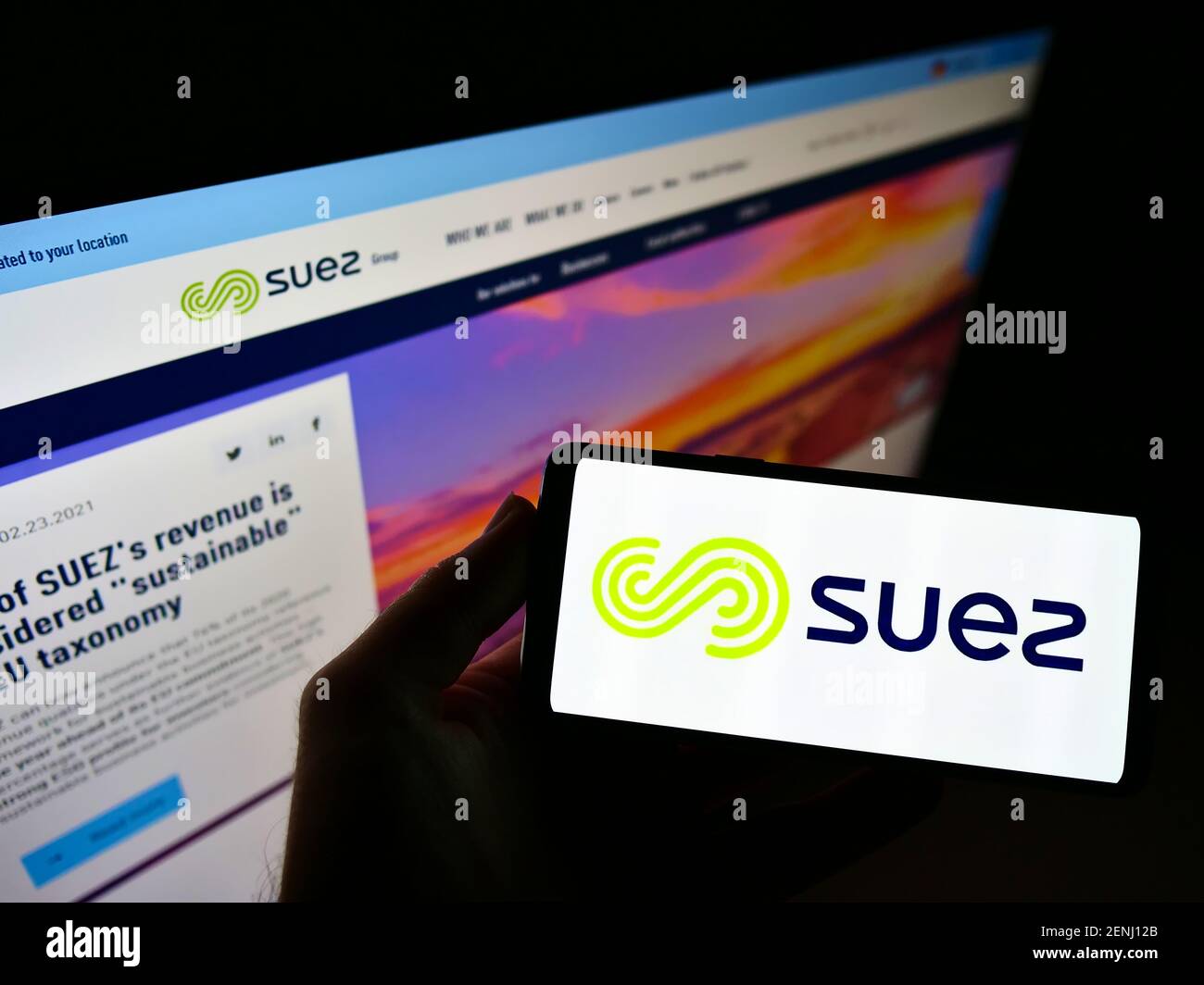 High angle view of person holding cellphone with logo of French utility company Suez SA on screen in front of website. Focus on mobile phone display. Stock Photo