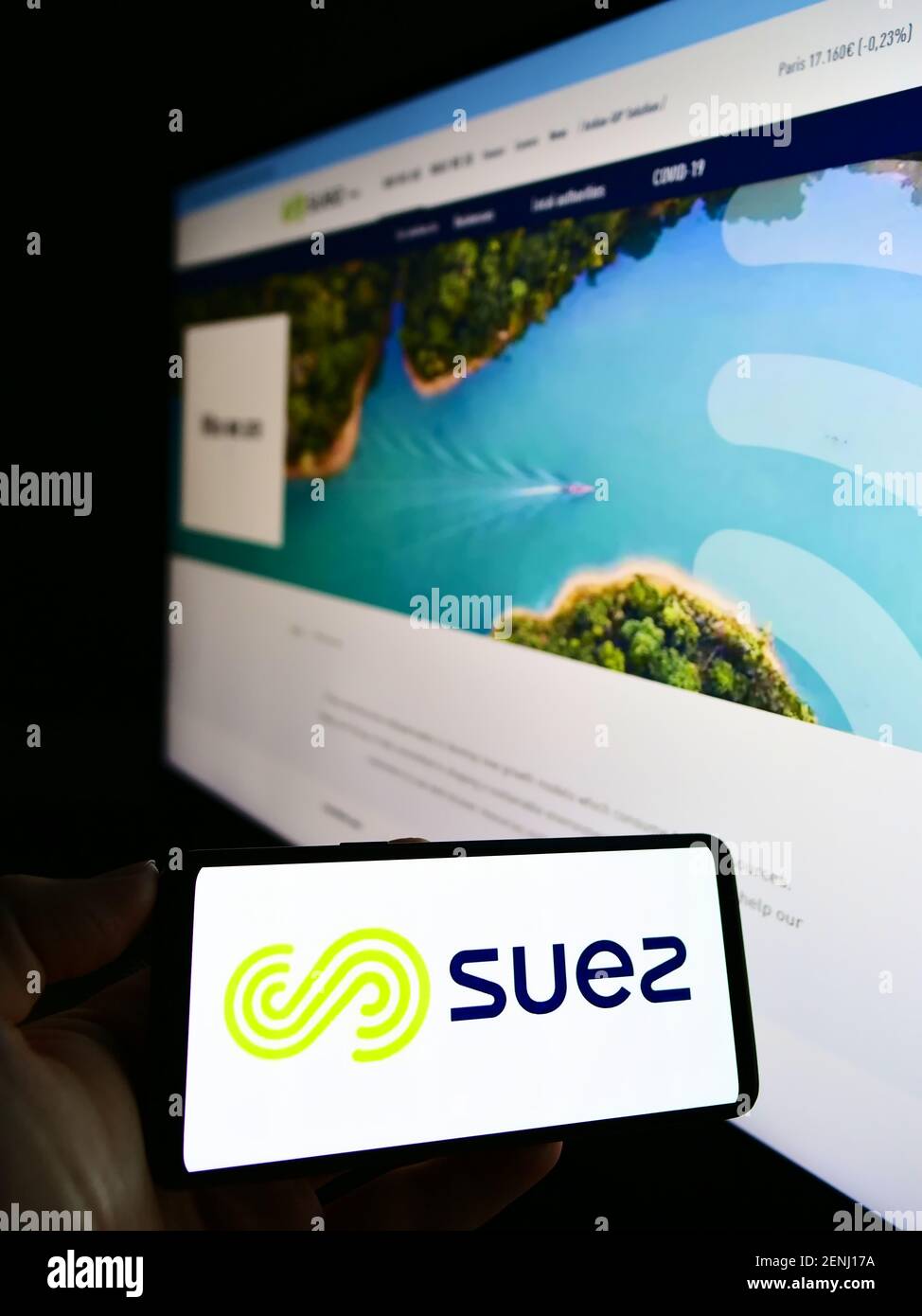 Person holding mobile phone with business logo of French utility company Suez S.A. on screen in front of web page. Focus on cellphone display. Stock Photo