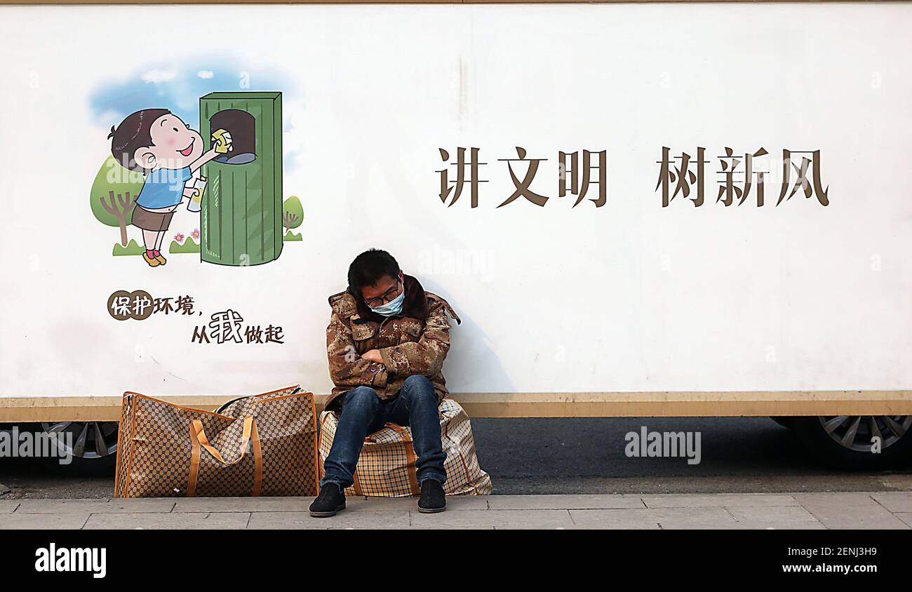 Beijing, China. 26th Feb, 2021. A Chinese man sits on his luggage at a long-distance bus station next to a banner promoting being a good citizen in downtown Beijing on Friday, February 26, 2021. China's President Xi Jinping claimed last year it had met a long-term target of lifting all its people out of extreme poverty. Photo by Stephen Shaver/UPI Credit: UPI/Alamy Live News Stock Photo