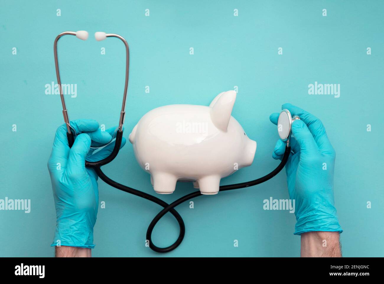 Health care cost. Doctor in surgical gloves holding a white piggy bank and stethoscope Stock Photo