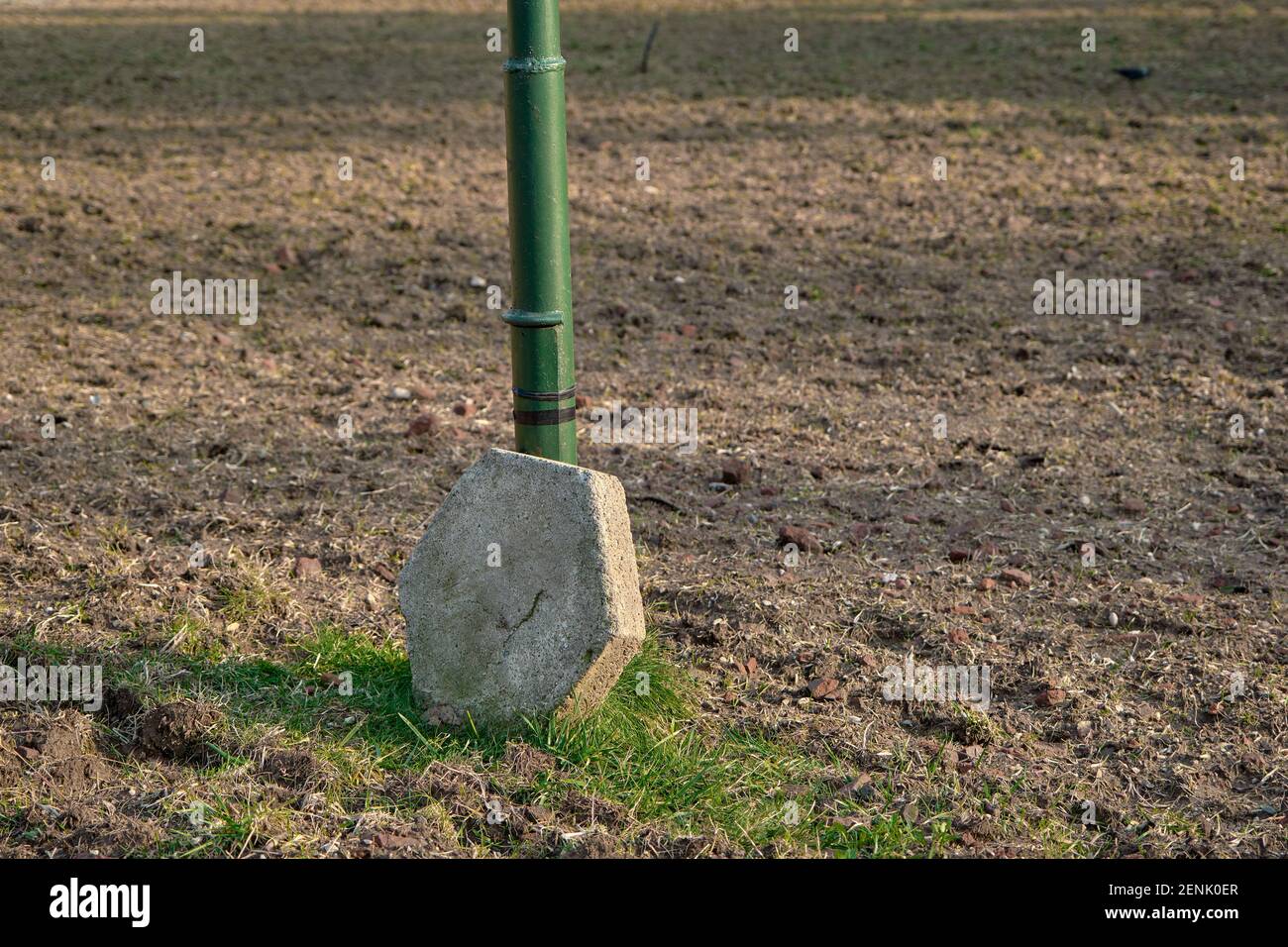 A stone shaped as hexagonal type and supported by green street lamps. Stone standing on soil and mud. Stock Photo