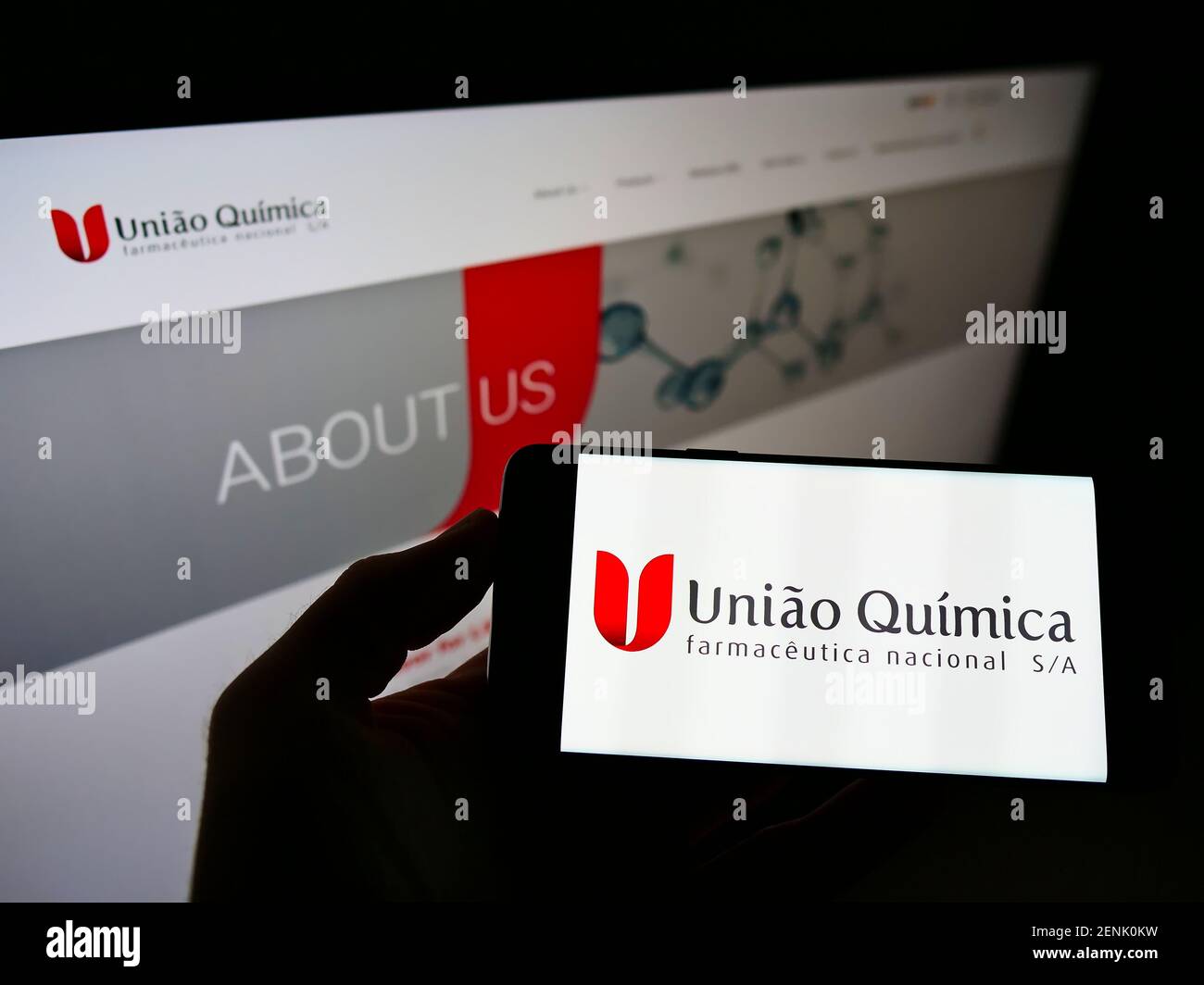 Person holding smartphone with logo of company União Química Farmacêutica Nacional S.A. on screen in front of website. Focus on phone display. Stock Photo