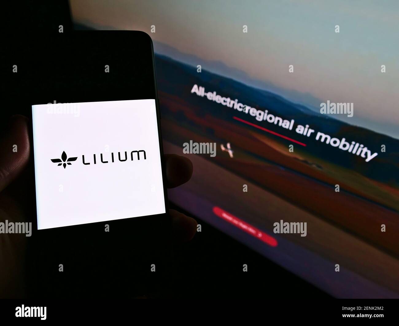 Person holding smartphone with logo of German airplane manufacturer Lilium GmbH (Lilium Jet) on screen in front of website. Focus on phone display. Stock Photo