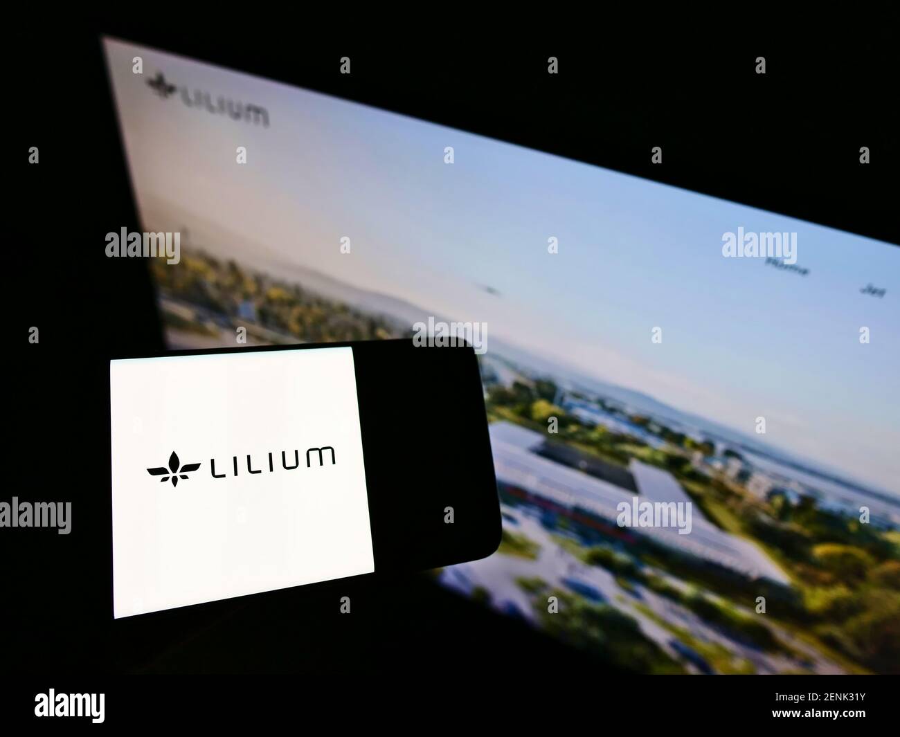 Person holding mobile phone with logo of German aircraft manufacturer Lilium GmbH (Lilium Jet) on screen in front of webpage. Focus on phone display. Stock Photo
