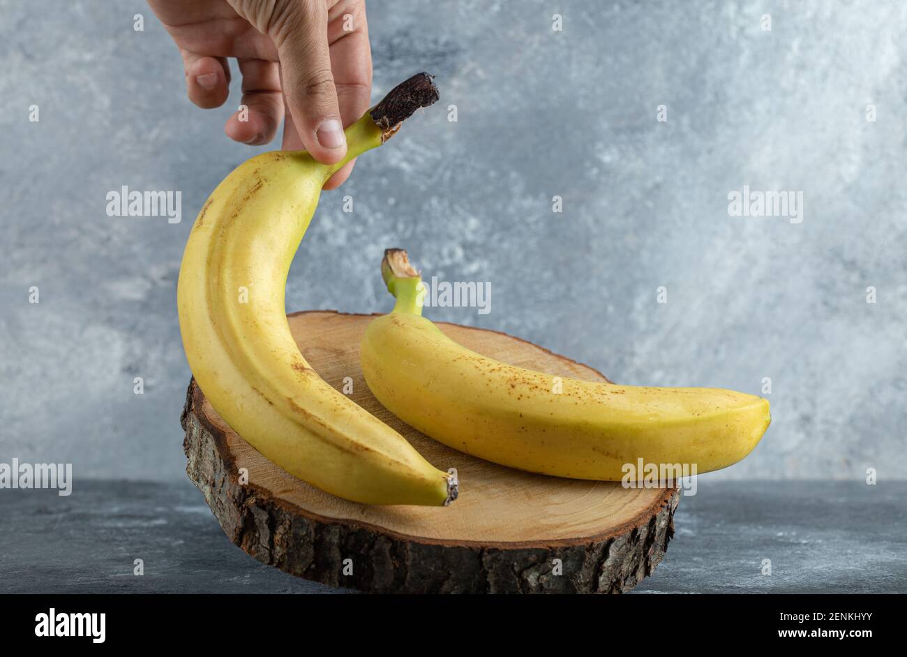 Female hand taking banana from wooden board Stock Photo