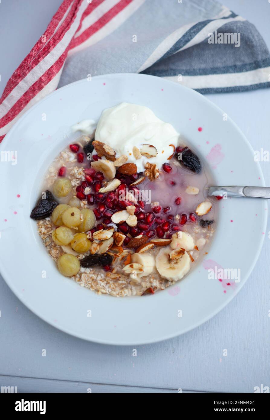 Bowl of meusli, nuts and fruit including pomegranates, banana slices,fat free yoghurt and gooseberries Stock Photo