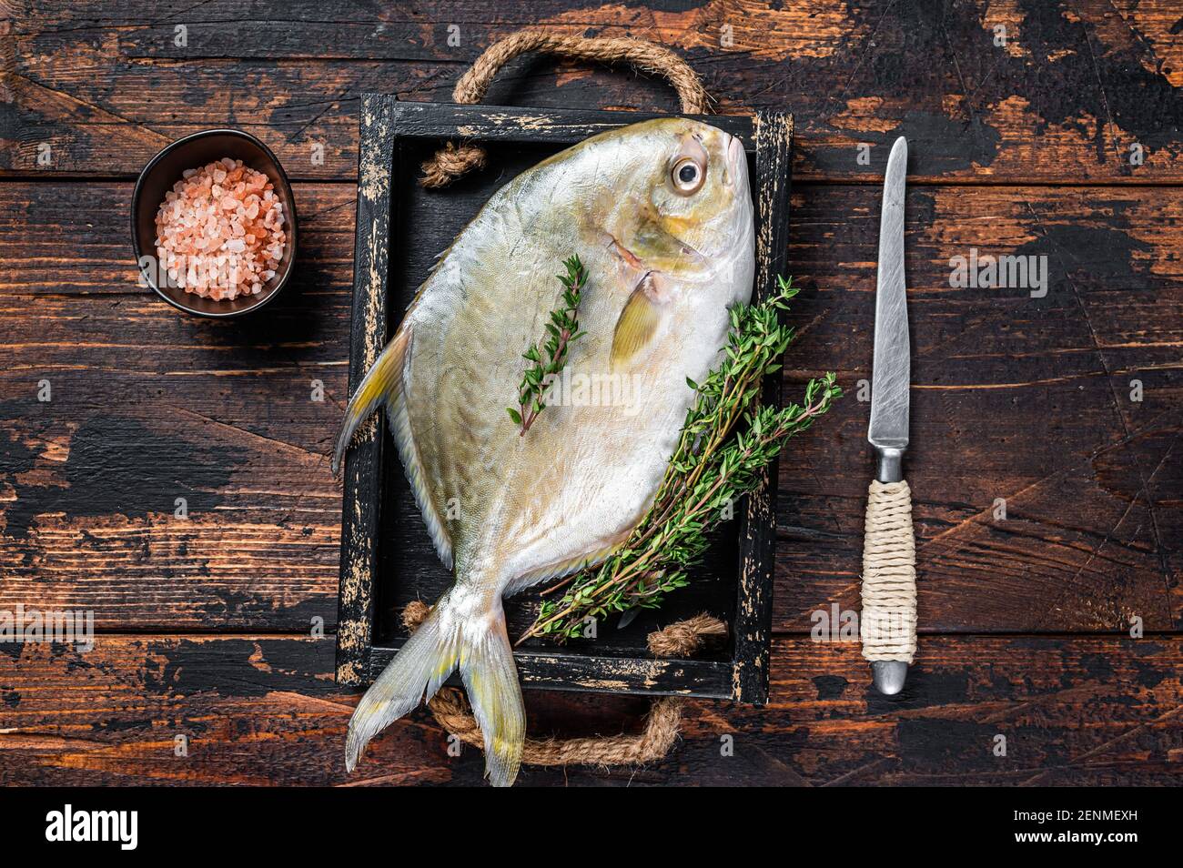 Raw fish butterfish or pompano with herbs in a wooden tray. Dark wooden background. Top view Stock Photo
