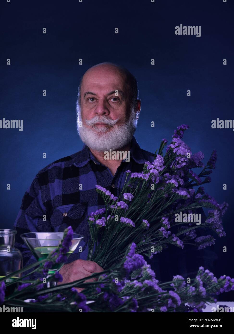 Portrait of elderly man in blue tones holding a bouquet of blue and purple flowers Stock Photo
