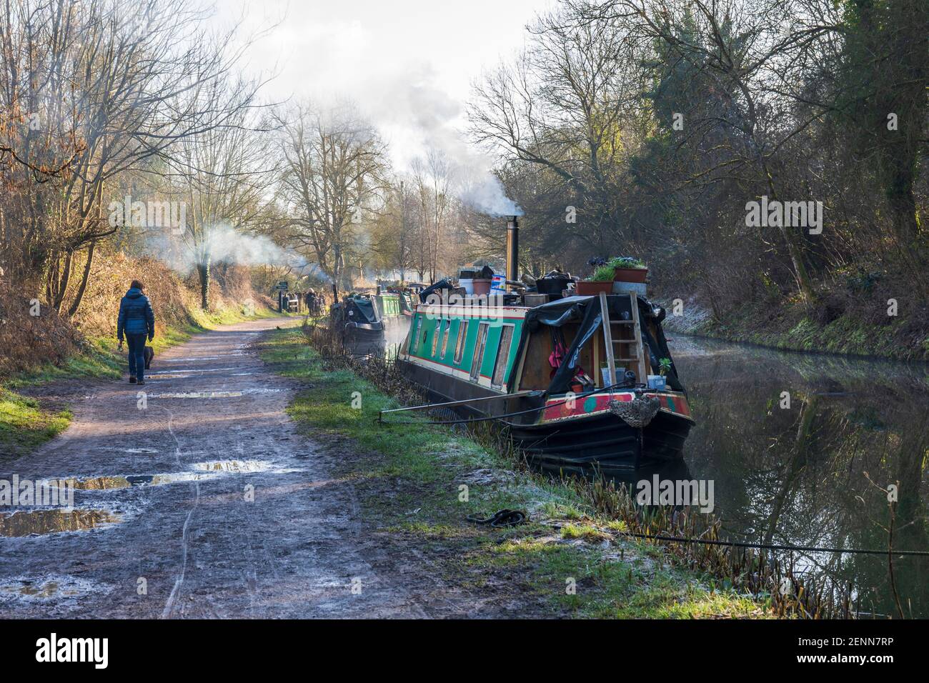 Walker by the canal boats moored beside the towpath of the Kennet and Avon canal on a bright winter day. Bradford on Avon, Wiltshire, England, UK Stock Photo