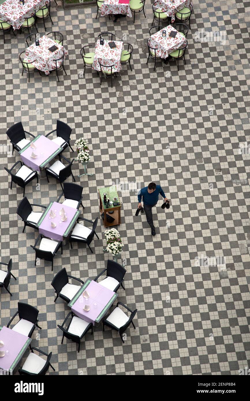 waiter crossing a piazza set with restaurant table and chairs Stock Photo