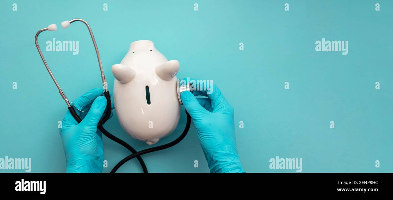 Health care cost. Doctor in surgical gloves holding a white piggy bank and stethoscope Stock Photo