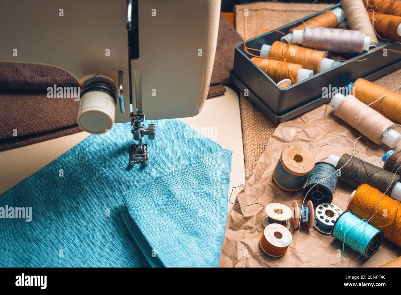 Thread, scissors, and fabric against a blurry sewing machine. Top view. Stock Photo