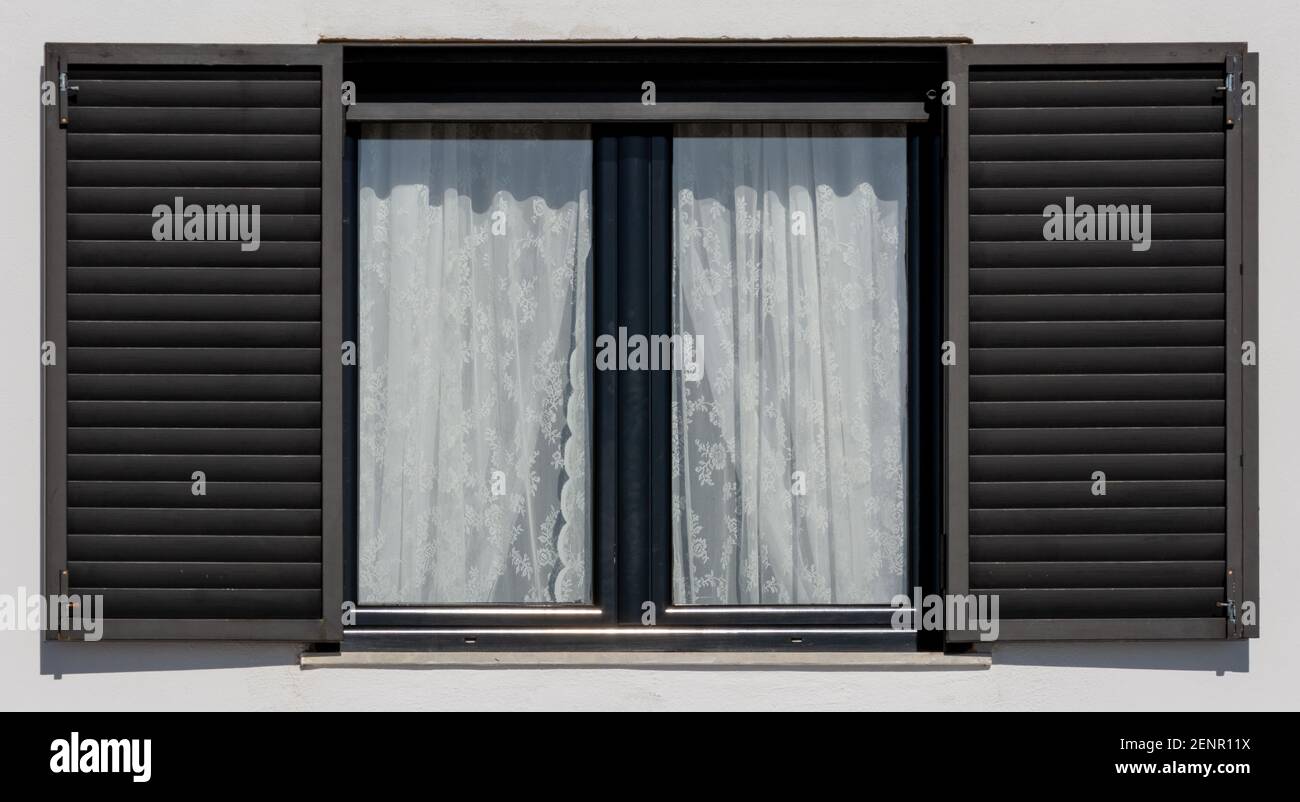 Wooden window with black shutters on a white facade Stock Photo