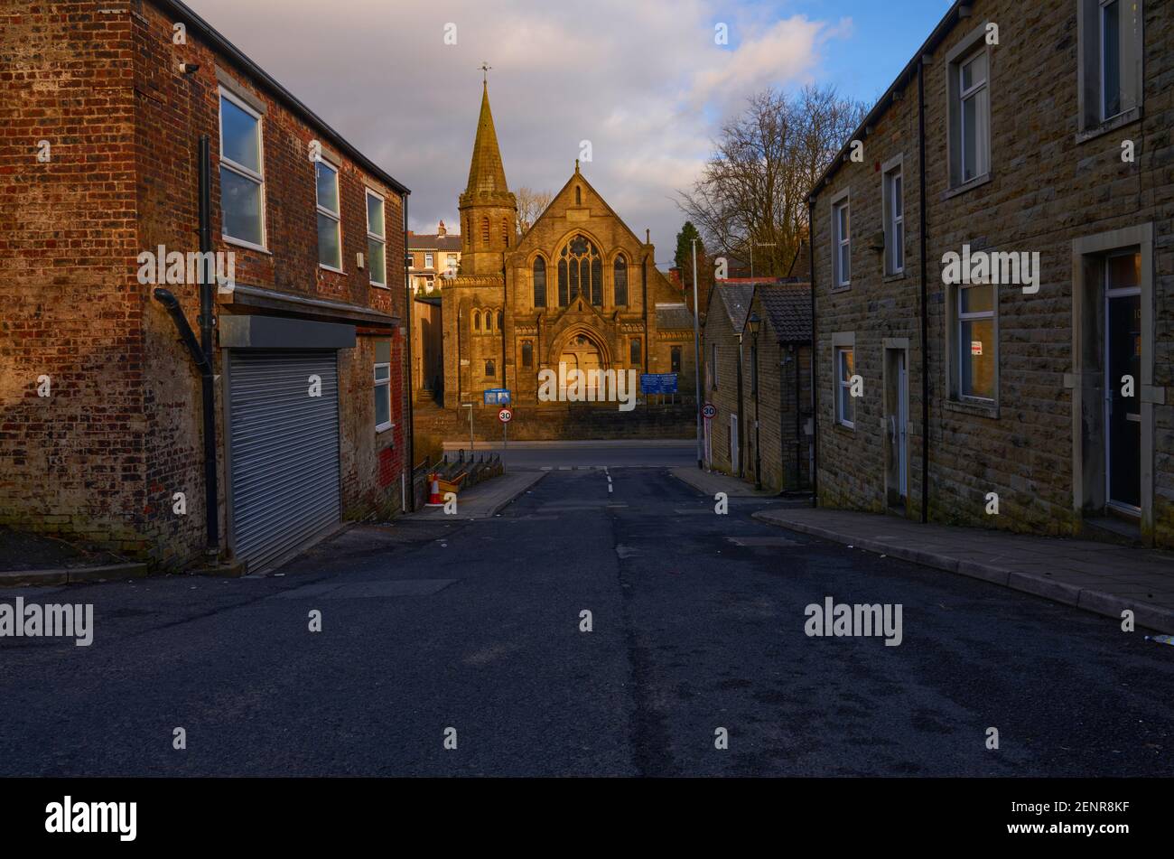 As the sun gets low over a northern town, the stone built church at the end of the street is illuminated in a beautiful yellow light Stock Photo