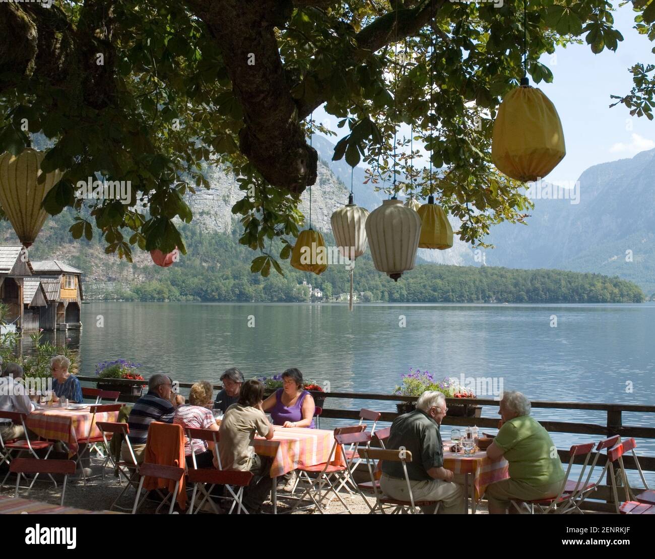 people at outdoor dining area at the lakeside of Hallstatt village shaded by chestnut trees with colourful lanterns, Hallstatt, Austra Stock Photo