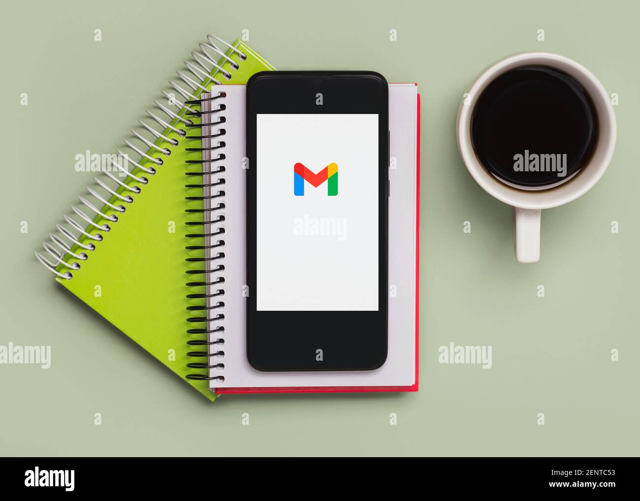 Gmail logo on black screen of smartphone with notebooks and cup of coffee on green background Stock Photo