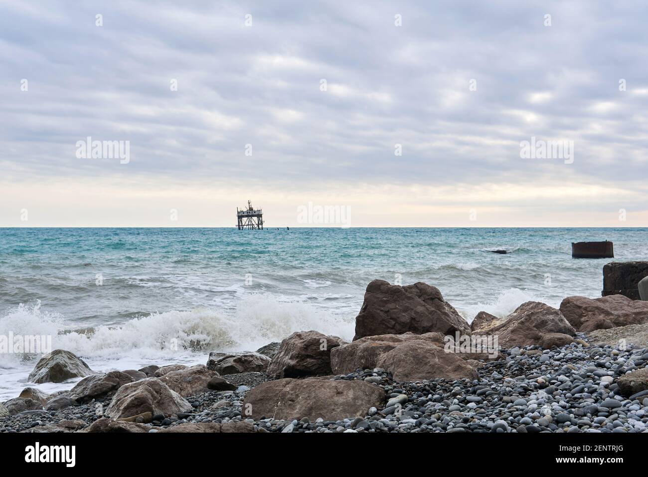 winter beach with seascape and a rickety structure on the stilts of an mariculture farm in the distance Stock Photo