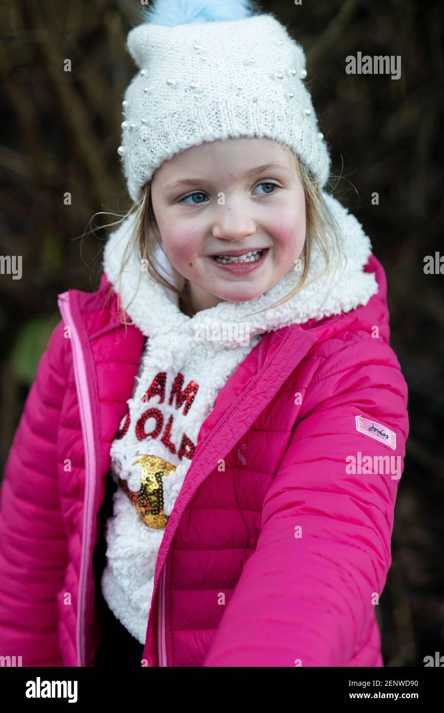 Little girl in pink winter coat and white woolie hat laughing and looking away from camera, 5 year old on a winter walk in Woodbridge Stock Photo