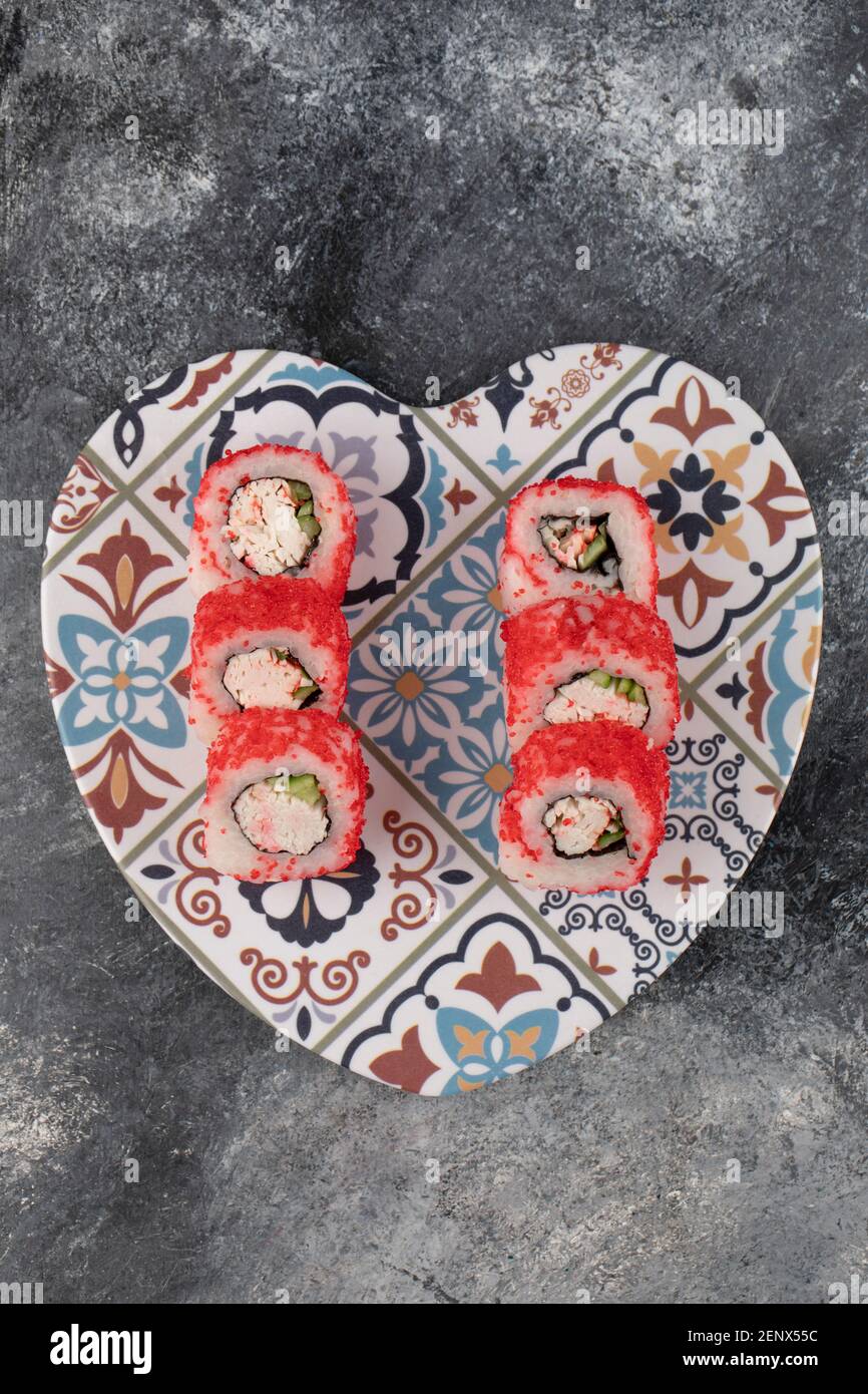 Tasty sushi rolls with red caviar on heart-shaped plate Stock Photo