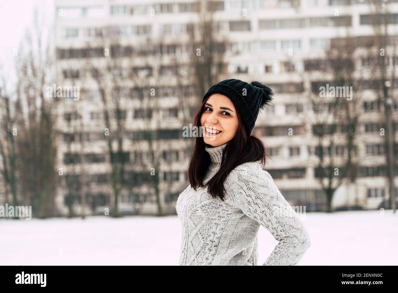 Young, beautiful woman with winter cap and gray sweater smiling and laughing while standing outside in winter. Stock Photo