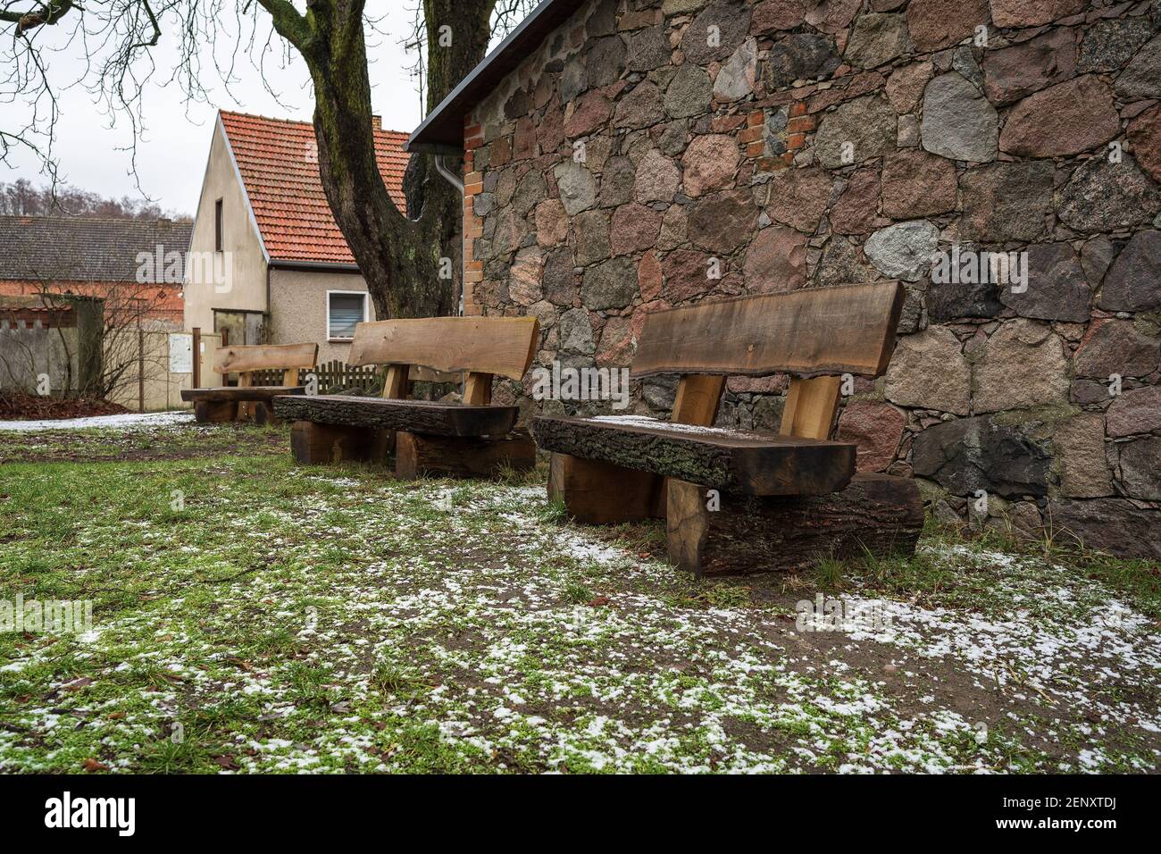 Oak benches near a stone wall. Wet snow on the ground. Stock Photo