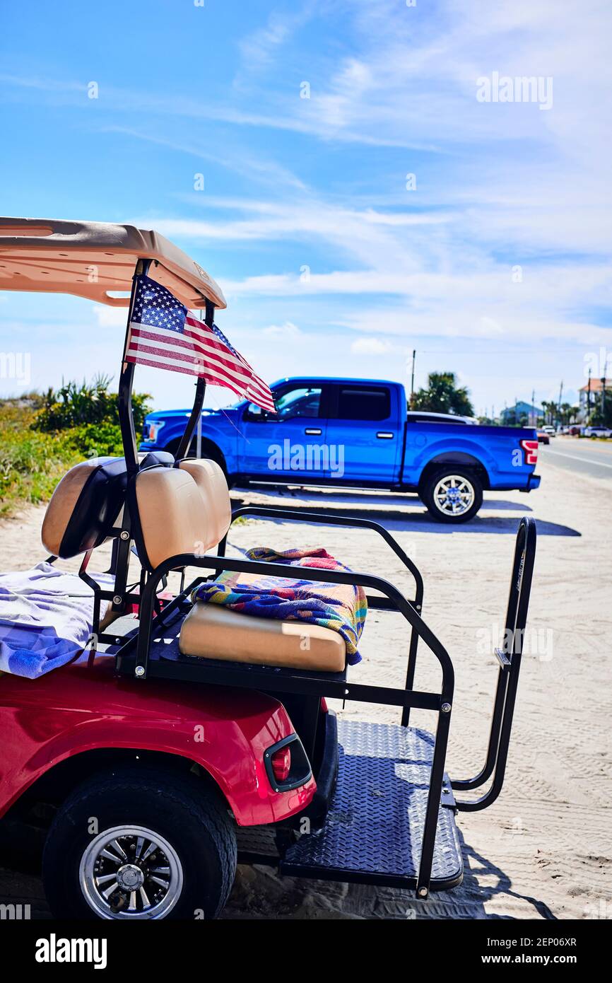 Golf cart parked at beach with american flag and pickup truck behind