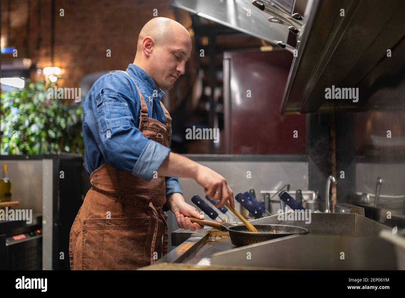 https://c8.alamy.com/comp/2EP06YM/bald-man-with-spoon-frying-dish-on-hot-pan-on-stove-during-work-in-cafe-kitchen-2EP06YM.jpg