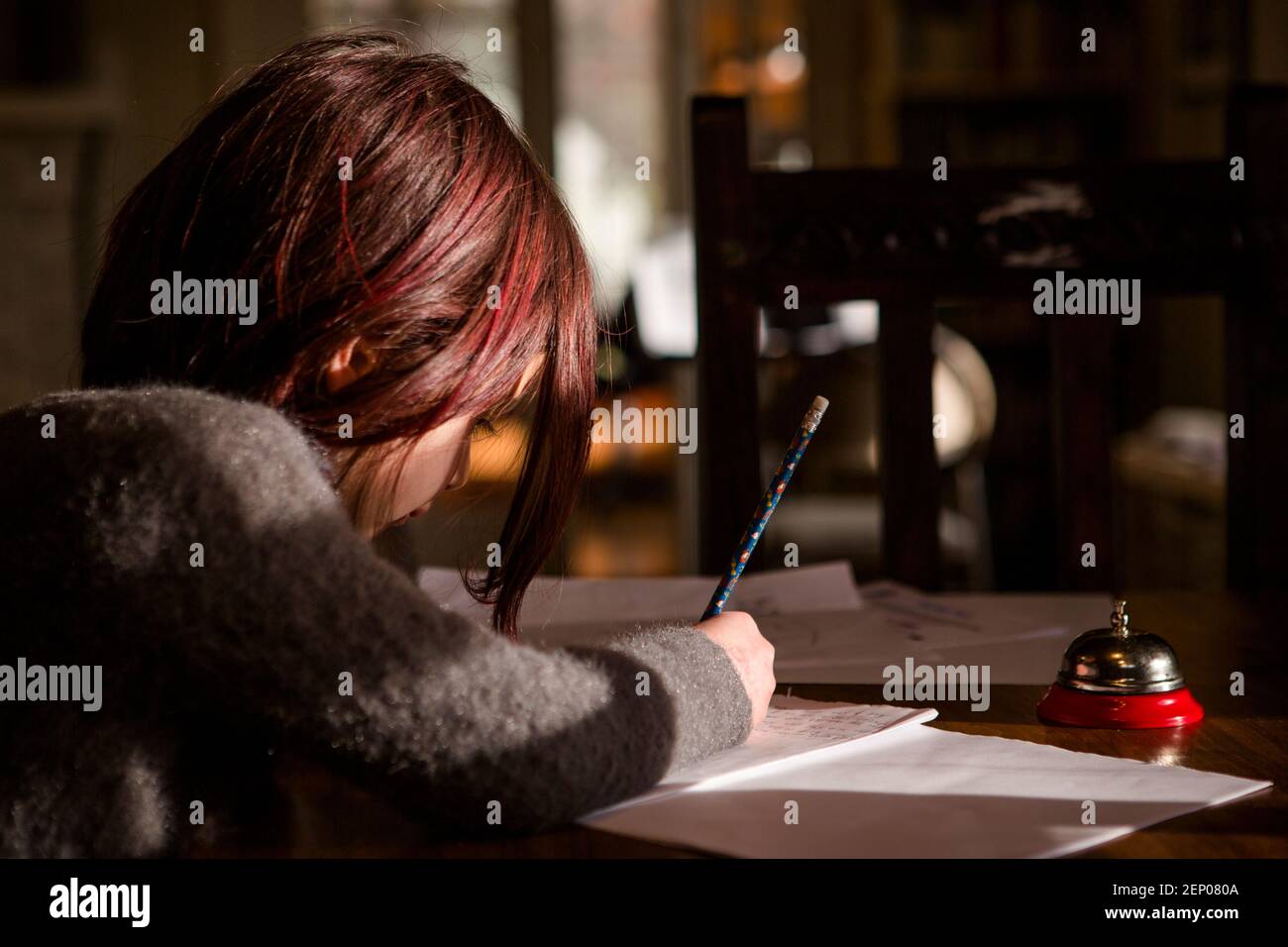 Little girl with bright red hair sits in patch of light writing story Stock Photo
