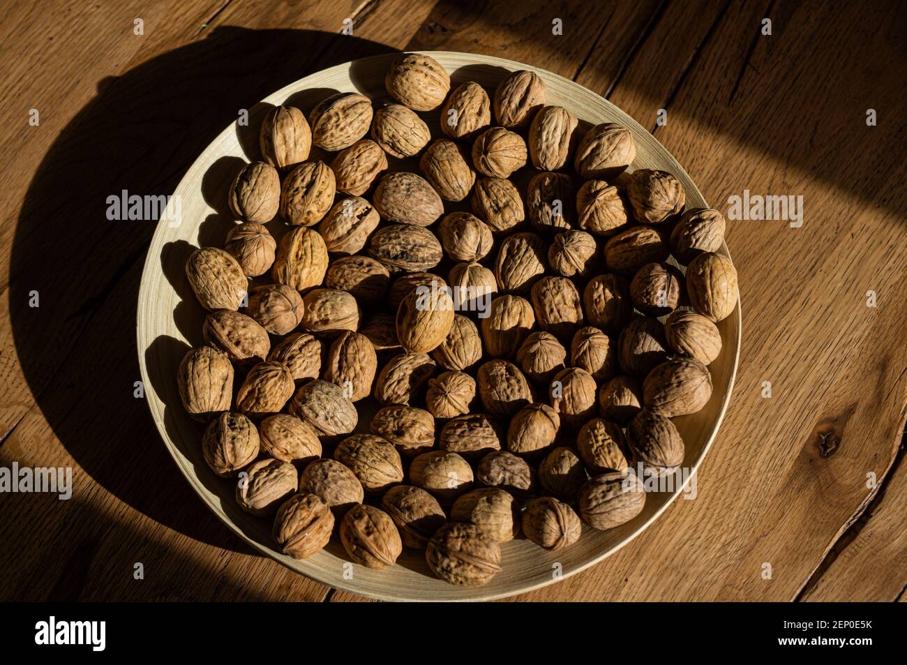 Plate of walnuts standing on a wooden table in a hard light Stock Photo