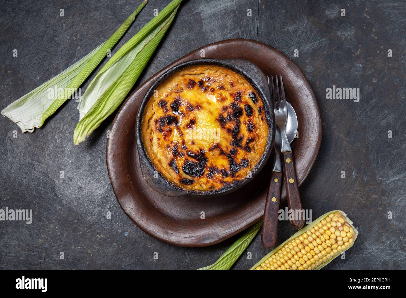 Chilean food. Traditional Pastel de Choclo corn pie. Beef meat with onion, chicken and egg covered with ground corn in clay bowl, top view Stock Photo