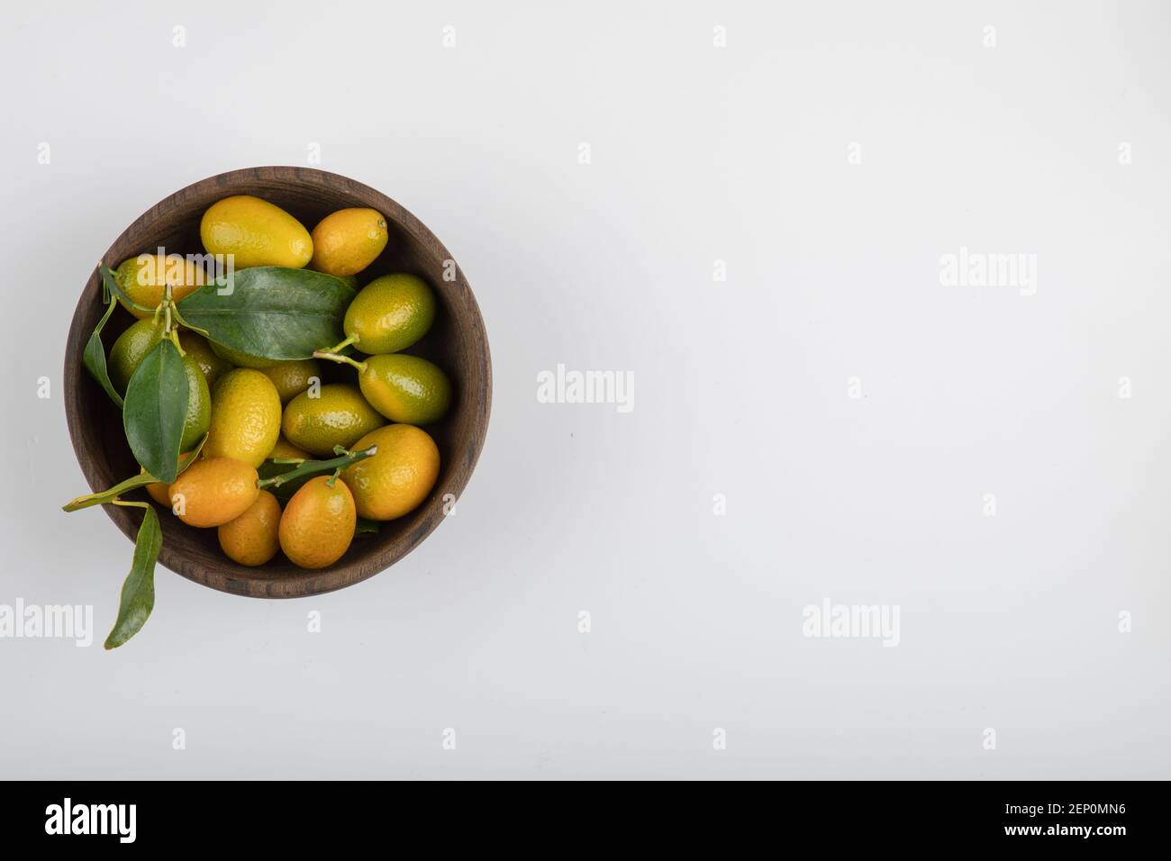 Wooden bowl of yellow kumquats with leaves on white background Stock
