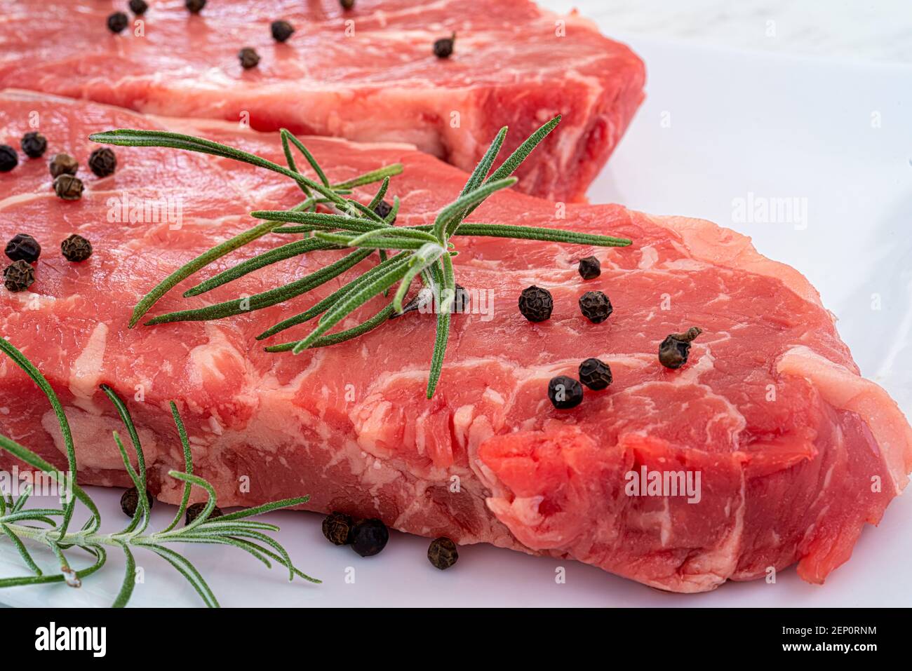 Marbled beef striploin steak garnished with rosemary and peppercorns on a white plate. Stock Photo