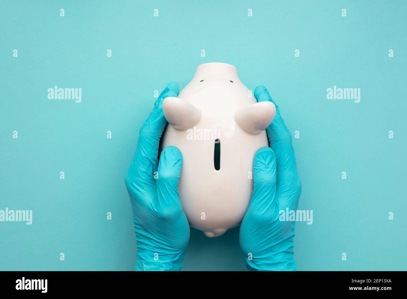 Health care cost. Doctor in surgical gloves holding a white piggy bank Stock Photo