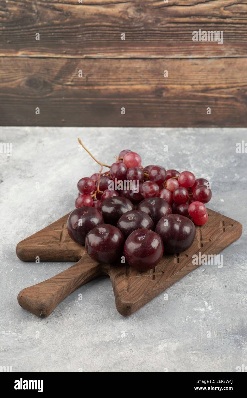 Wooden board of fresh red plums and grapes on marble surface Stock Photo