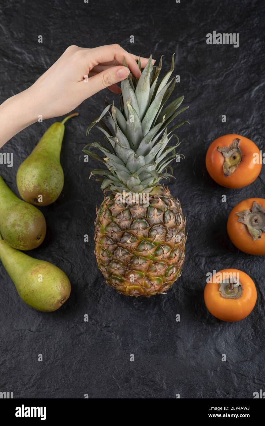 Female hand holding ripe pineapple on black surface Stock Photo