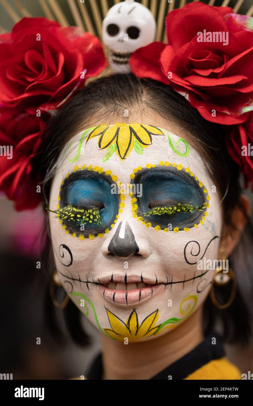 A woman with a brightly colored Catrina face paint poses for the camera  during the Catrina Festival. Thousands of people took to the streets of  Mexico City to watch the procession of
