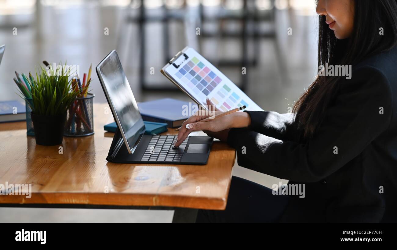 Cropped shot of young female designer or graphic designer working with computer tablet on wooden office desk. Stock Photo