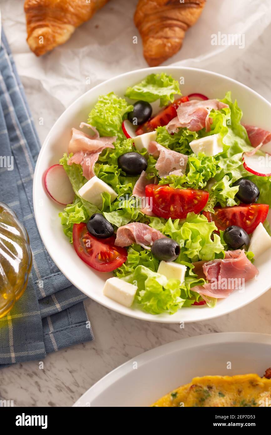 Healthy salad in a bowl with olives, raddishes, tomato, cheese and lean ham served for breakfast Stock Photo