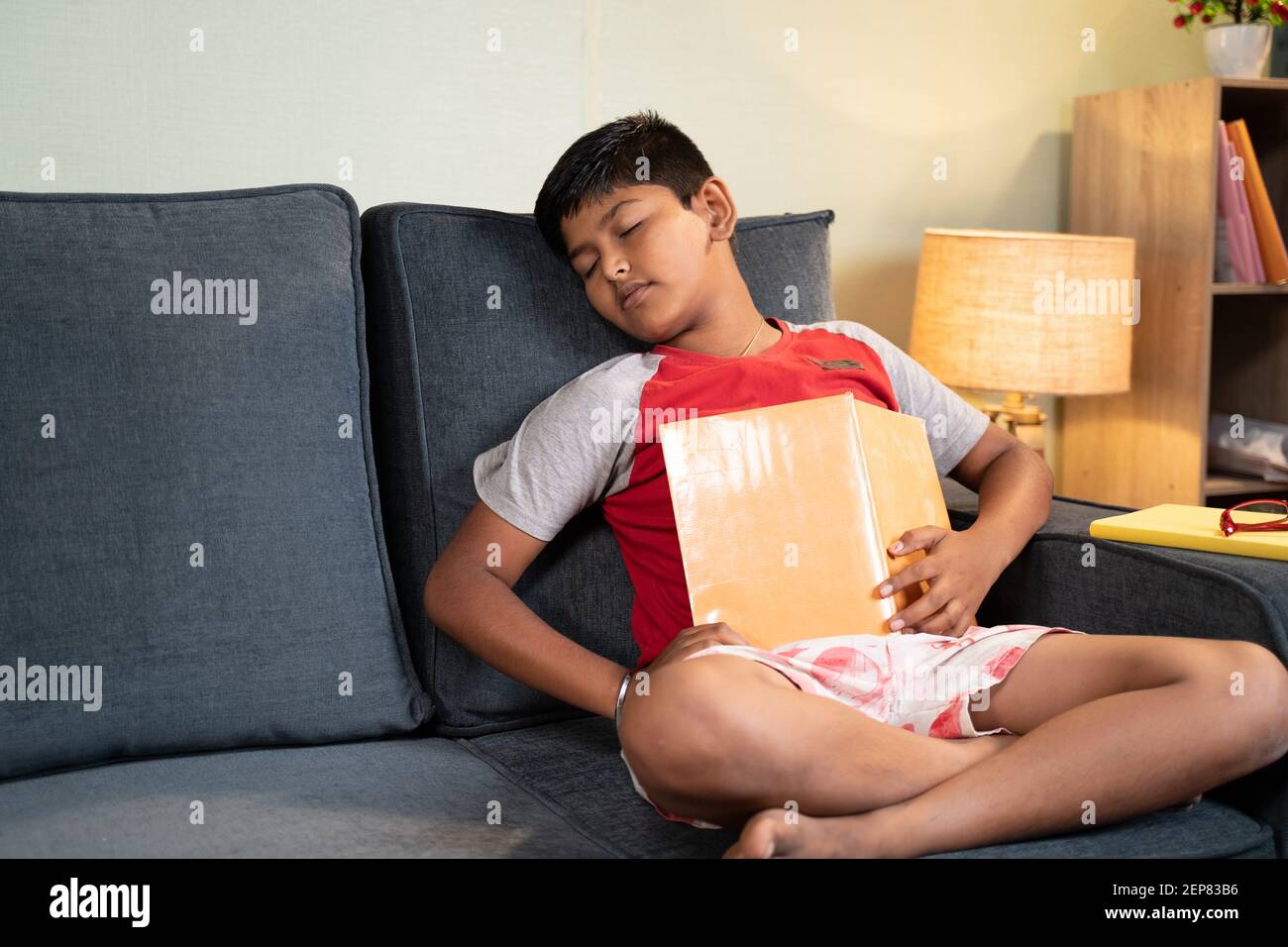 Tired kid sleeps while busy reading book for examination on sofa - concept of lazy, not interested preschool children Stock Photo