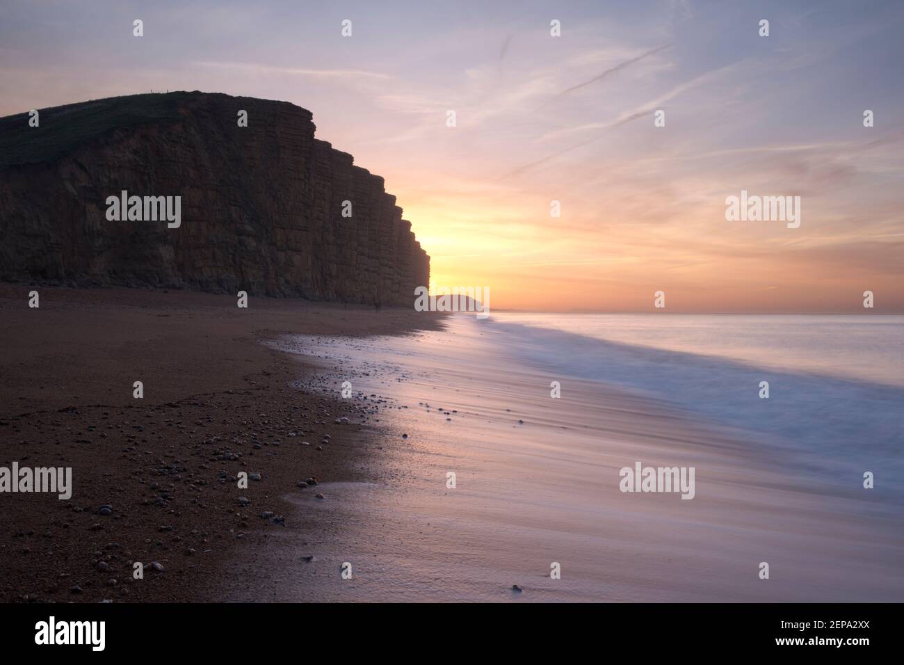 Sunrise over East Cliff while the tide laps the beach at West Bay, Dorset, UK. Stock Photo
