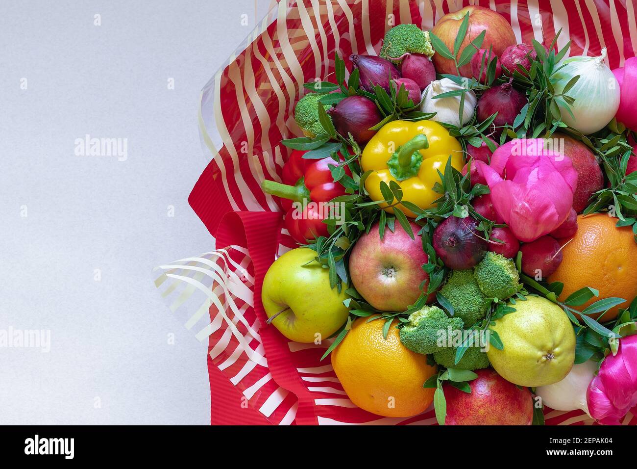 A stunning colorful bouquet of various fresh fruits, vegetables and flowers surrounded by red and transparent with white striped paper on a beige back Stock Photo
