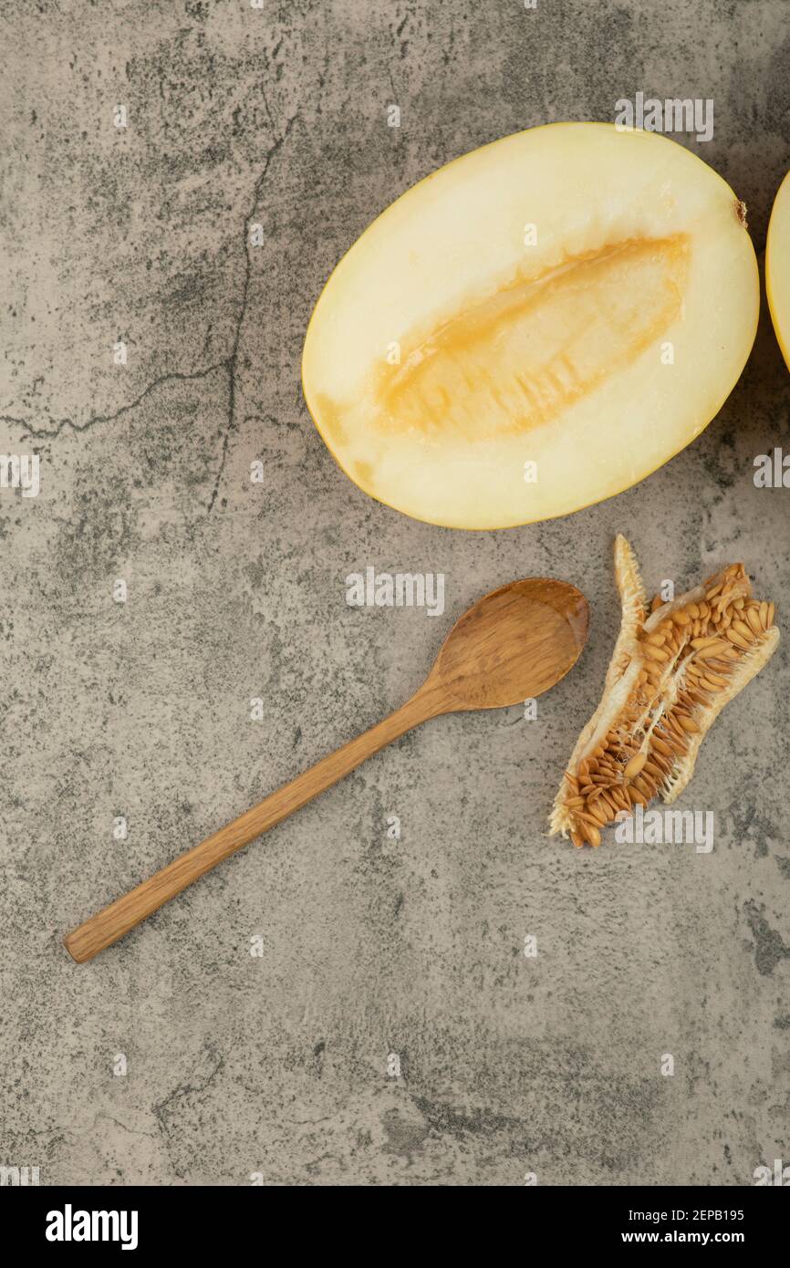 Halved delicious yellow melons on marble surface with wooden spoon aside Stock Photo
